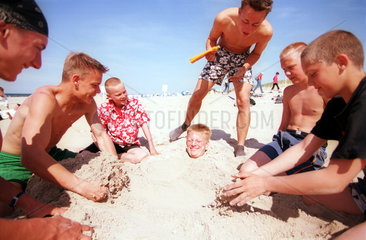 Ein Junge steckt bis zum Hals eingebuddelt im Sand