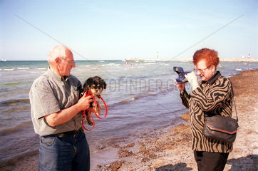 Frau fotografiert ihren Mann mit Hund an der Ostsee