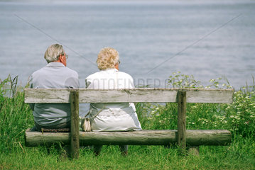 Rentnerpaar sitzt auf einer Bank am Wasser