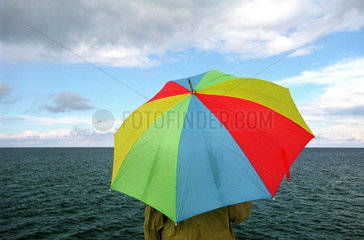 Mann unter buntem Regenschirm am Meer