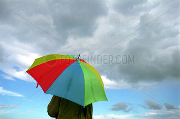 Mann unter buntem Regenschirm und wolkiger Himmel