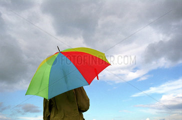 Mann unter buntem Regenschirm und wolkiger Himmel