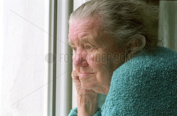 Alte Frau schaut aus Fenster  Brandenburg