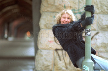 Lachende junge Frau haengt an Laternenpfahl  Berlin
