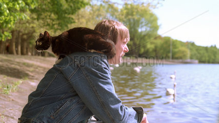 Mann sitzt mit Katze auf der Schulter am See