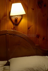 Schirmlampe ueber einem Bett an einer holzvertaefelten Wand