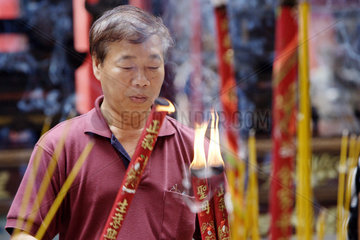 Vietnam  ein Mann zuendet Raeucherstaebe im Thien-Hau-Tempel an