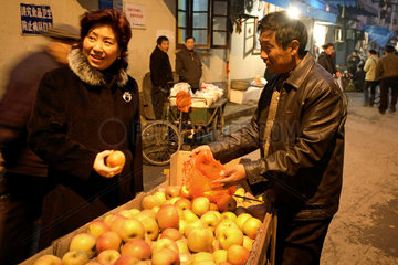 Shanghai  Frau kauft Aepfel bei einem Strassenhaendler