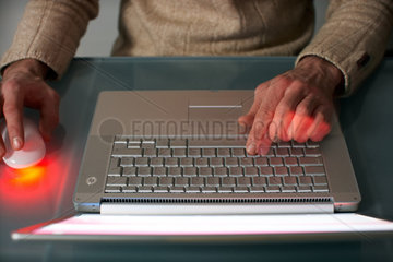 Ein Mann sitzt an einem Glastisch mit einem Laptop