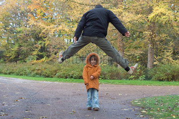 Ein Mann springt ueber ein Kind im Park