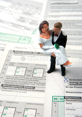 Brautpaar als Miniaturfiguren auf Steuerformularen stehend