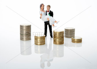 Ein Brautpaar als Miniaturfiguren mit Stapeln von Euromuenzen