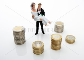Ein Brautpaar als Miniaturfiguren mit Stapeln von Euromuenzen
