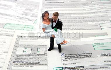 Brautpaar als Miniaturfiguren auf Steuerformularen stehend