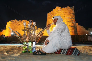 Dubai  ein Mann raucht eine Wasserpfeife in der Wueste
