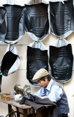 Vietnamesischer Schneider sitzt im Freien an seiner alten Naehmaschine und naeht