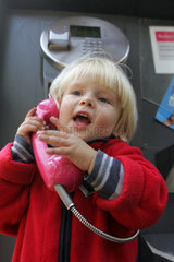 Berlin  ein Kleinkind beim Telefonieren in einer Telefonzelle