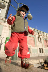 Berlin  Kleinkind mit Muetze und Sonnenbrille balanciert auf einer Mauer
