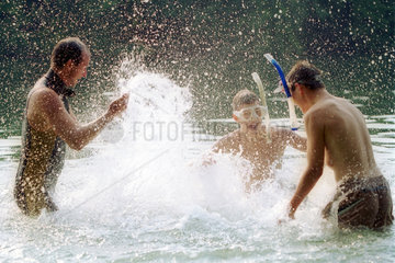 ein Mann und zwei Jungen bespritzen sich mit Wasser