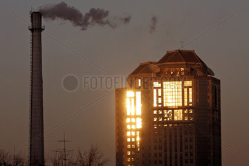 Symbolfoto  qualmender Fabrikschornstein mit einem in der Sonne leuchtenden Wohnhaus