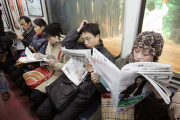 Peking  Fahrgaeste in der U-Bahn beim Zeitung lesen