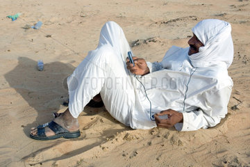 Dubai  arabischer Mann liegt in der Wueste und ist mit seinem Mobiltelefon beschaeftigt