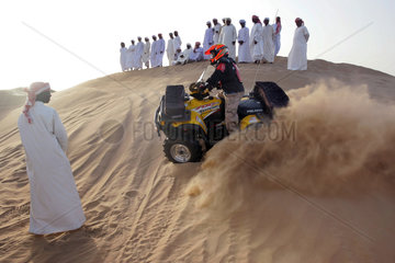 Dubai  eine Gruppe arabischer Maenner beobachtet einen Quadfahrer in der Wueste