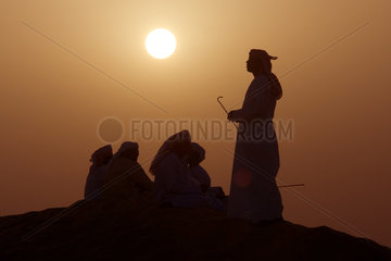 Dubai  arabische Maenner in der Wueste bei Sonnenuntergang