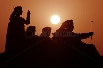 Dubai  arabische Maenner in der Wueste bei Sonnenuntergang