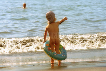 Ein Kind mit Schwimmring am Strand in den Ferien