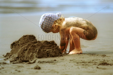 Kind spielt mit Sand am Strand in den Ferien