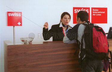 Eine Angestellte von Swiss im Gespraech mit einem Reisenden beim Einchecken