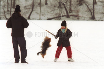 Kinder spielen auf einem zugefrorenen See im Winter mit einem Hund