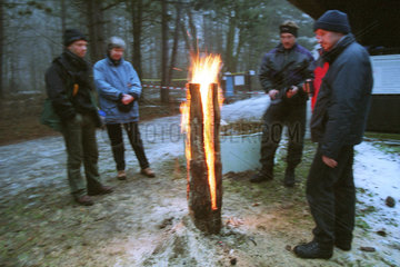 Eine Gruppe Menschen waermen sich an einer Feuerstelle im Winter