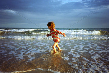 Ein Kind fluechtet vor den Wellen am Meer