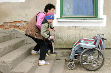 Eine Mutter hebt ihren Sohn in den Rollstuhl