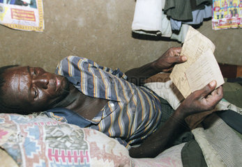 Bettlaegeriger Aidspatient schaut auf sein Krankenblatt