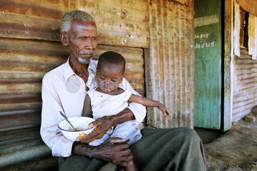 Grossvater mit seinem Enkel vor einer Wellblechhuette