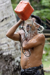 Ein Mann uebergiesst sich mit einem Eimer Wasser