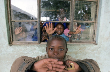 Afrikanische Schueler gestikulierenren aus  und vor dem Fenster eines Klassenraumes
