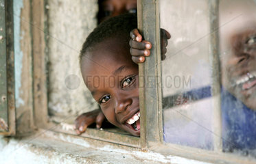Afrikanische Schueler lachen aus dem Fenster eines Klassenraumes