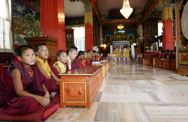 Junge buddhistische Moenche in Gewaendern sitzen in einem Kloster