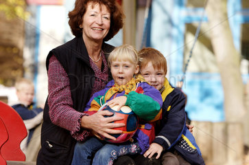 Berlin  eine Grossmutter sitzt mit mit zwei Kindern auf einem Kinderspielplatz