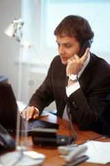 Mann sitzt am Schreibtisch im Buero und telefoniert