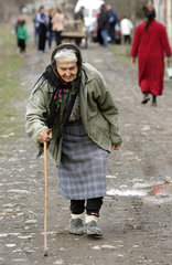 Eine alte Frau geht gebueckt auf einer Dorfstrasse