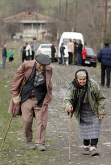 Eine alte Frau und ein alter Mann gehen gebueckt auf einer Dorfstrasse