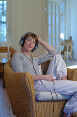 Junge Frau sitzt zu Hause in einem Korbsessel und hoert Musik mit einem MP3 Player