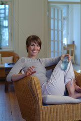 Junge Frau sitzt zu Hause mit einem Glas Wasser in einem Korbsessel