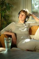 Junge Frau sitzt zu Hause in einem Korbsessel und hoert Musik mit einem MP3 Player