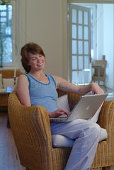 Junge Frau sitzt in einem Korbsessel und surft im Internet